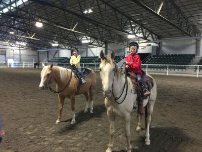 Two riders on horseback in an indoor arena.